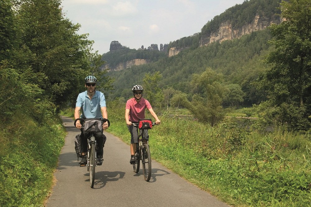 Fietspad met 2 fietsers met helmen en bergen er naast.